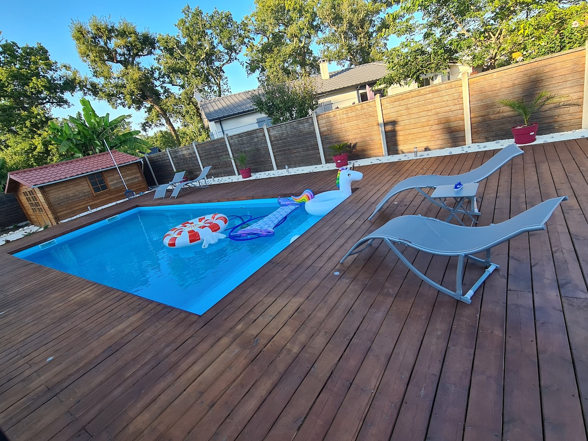 A spacious outdoor area features a heated swimming pool surrounded by a wooden deck. Colorful pool inflatables sit in the water, and lounge chairs are positioned for relaxation. Potted plants add greenery to the setting, creating a welcoming environment for leisure.
