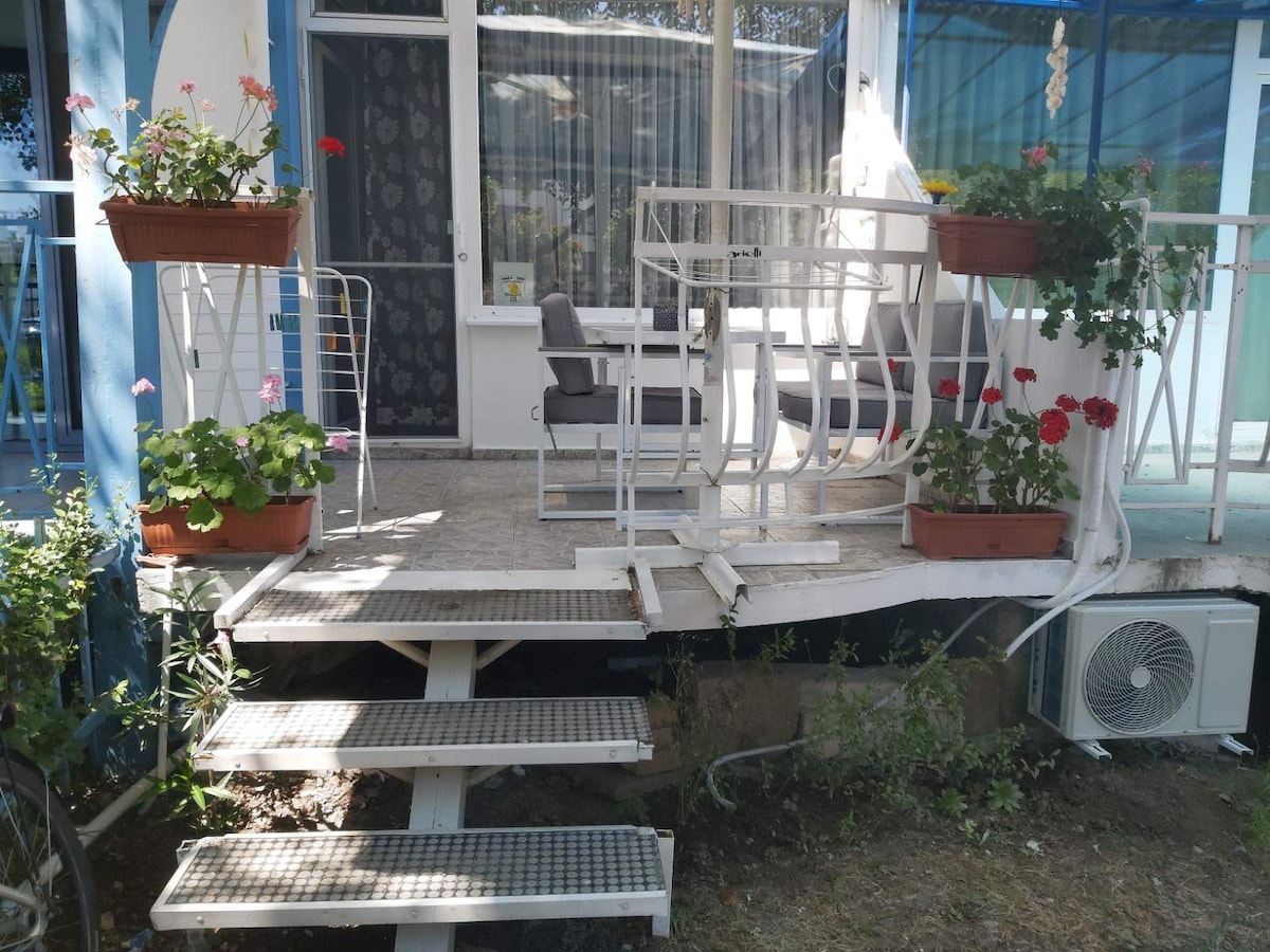 A welcoming outdoor area is highlighted by potted flowers, providing a touch of color. Steps lead up to a private entrance, where a small seating arrangement offers a place to relax. An air conditioning unit is visible beside the entryway.