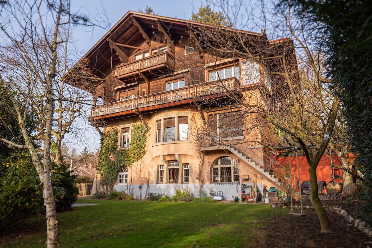 The villa is a charming three-story building with a mix of wood and stucco exterior. Large windows provide natural light, while the balcony adds a cozy touch. Surrounding greenery and a well-maintained garden create a serene setting, inviting relaxation and enjoyment of the outdoors.