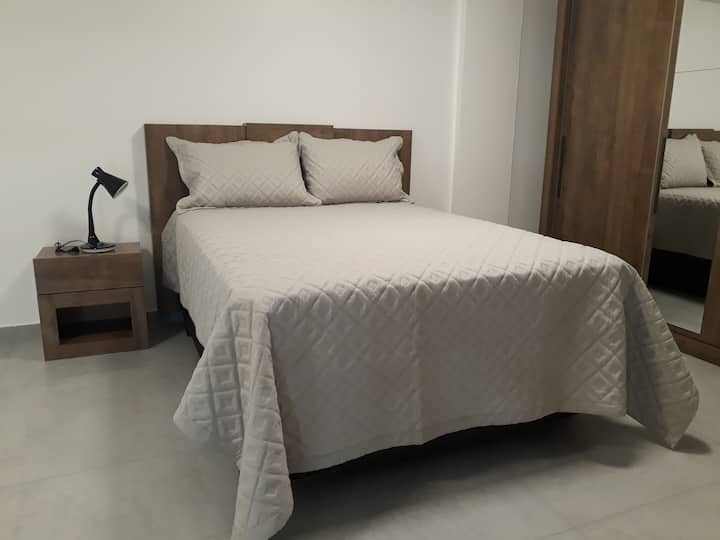 Habitación con cama doble, aire acondicionado, 2 mesitas de noche, lámpara de mesa, armario con espejo y perchas.