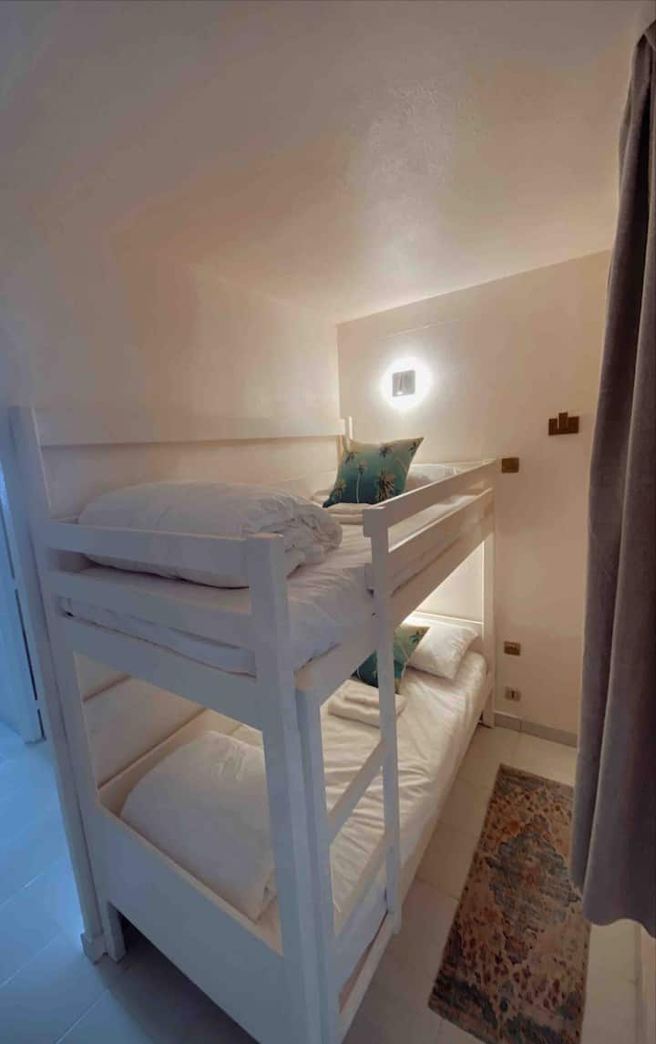 ¡La habitación de la litera! Un pequeño dormitorio con dos literas individuales. Cada cama tiene su propia luz de lectura. Hay una pequeña ventana con cortinas de cierre y una puerta que cierra este espacio de la sala de estar principal del apartamento.