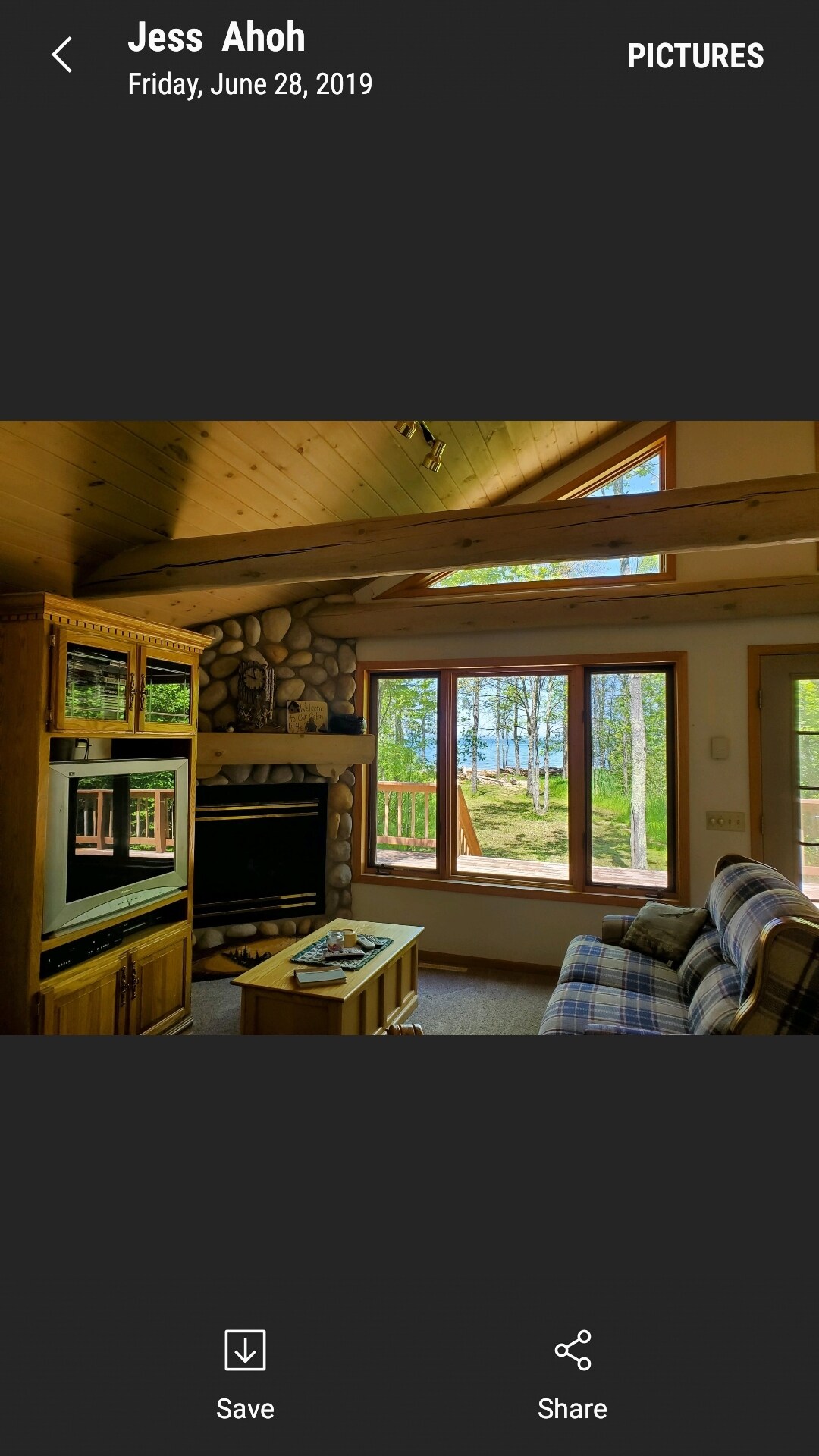 A light-filled living area features a combination of wood paneling and stone accents. Large windows offer views of the outdoors, while a cozy sofa and a wooden media center with a television create a comfortable space for relaxation.