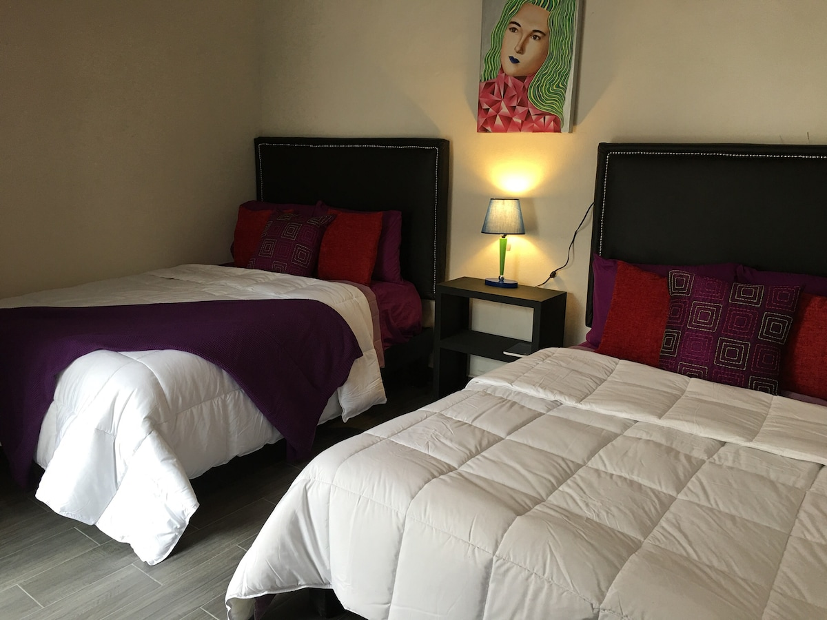 חדר שינה שני עם שתי מיטות זוגיות, כורסה/כיסא, ריהוט לאחסון בגדים או חפצים.