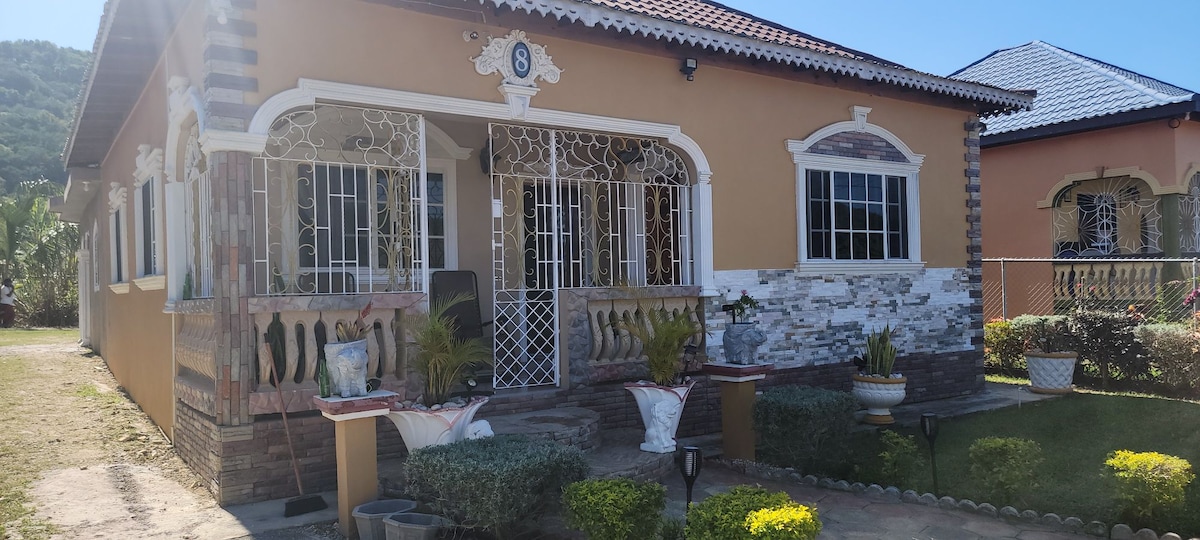 The villa's exterior showcases a charming facade with detailed stonework and decorative elements. A covered front porch is framed by wrought iron railings, and well-maintained shrubs and small flower pots enhance the inviting entryway.