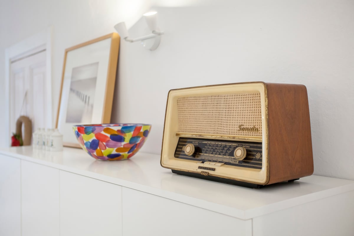 A vintage radio sits atop a sleek white dresser, complemented by a colorful decorative bowl. The background features framed artwork hanging on the wall, enhancing the aesthetic of the living space.