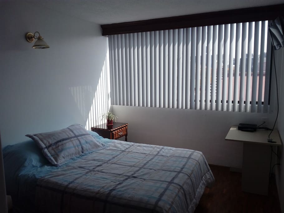Cama matrimonial con TV, escritorio y closet.