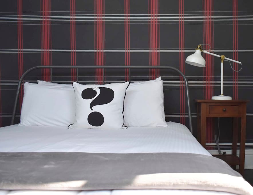 The Queen-sized bed is up against a full wall covered in modern plaid wall paper
