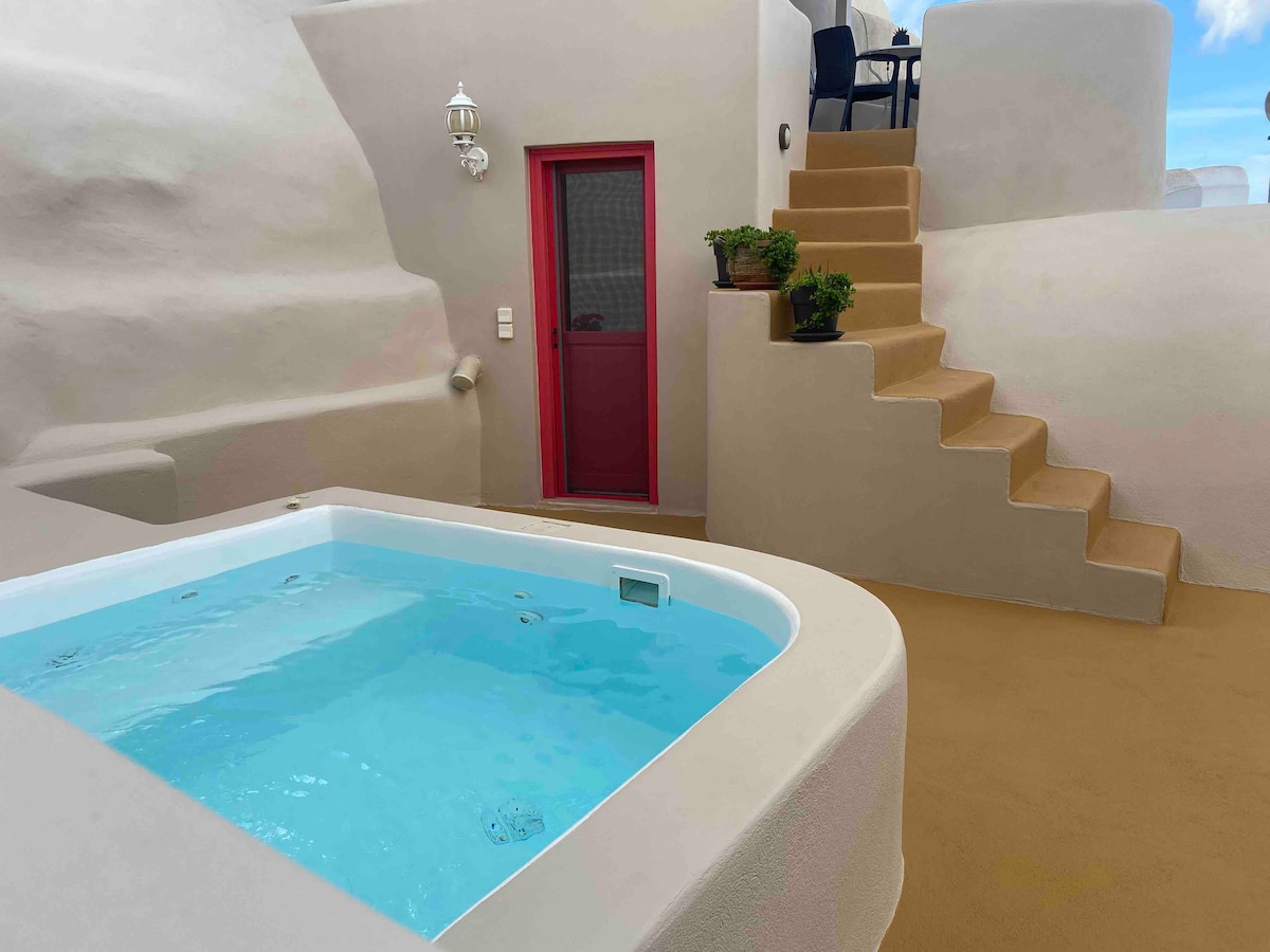 A private outdoor area features a small blue plunge pool, surrounded by smooth beige walls. A red door leads inside, while a set of stairs with potted plants ascends beside the pool, enhancing the natural cave-like design.