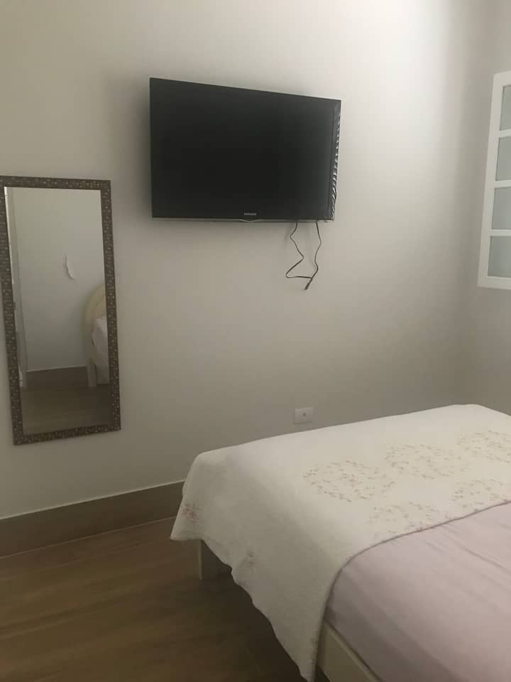 卧室套房配有双人床，宽敞通风。带架子和抽屉的储物柜、镜子、电视和空调。