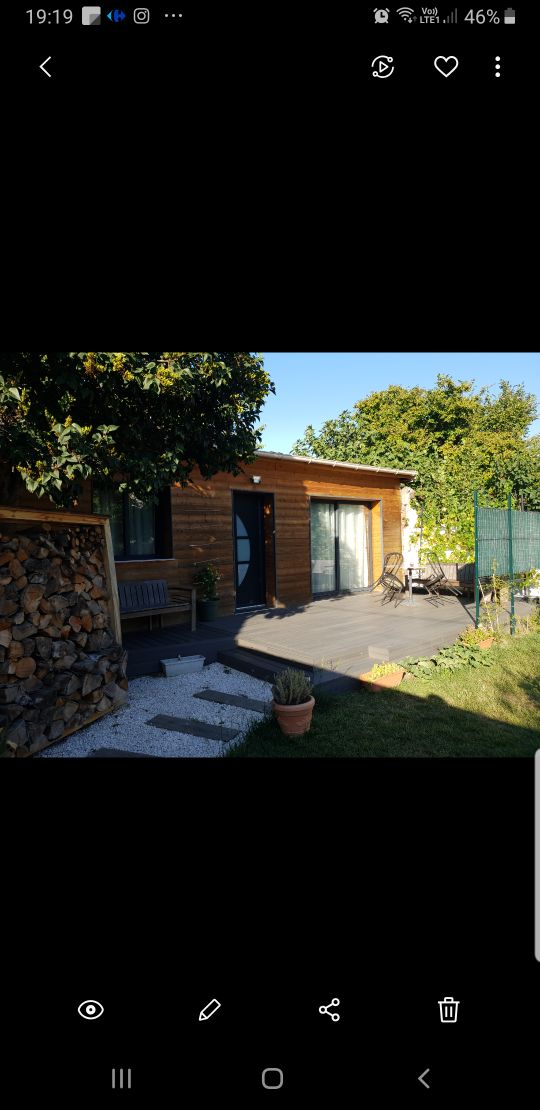 The exterior of the property features a wooden design with large glass doors leading to a garden area. A cozy seating arrangement is located on the patio, surrounded by greenery and a neatly stacked pile of firewood. Natural light illuminates the space.