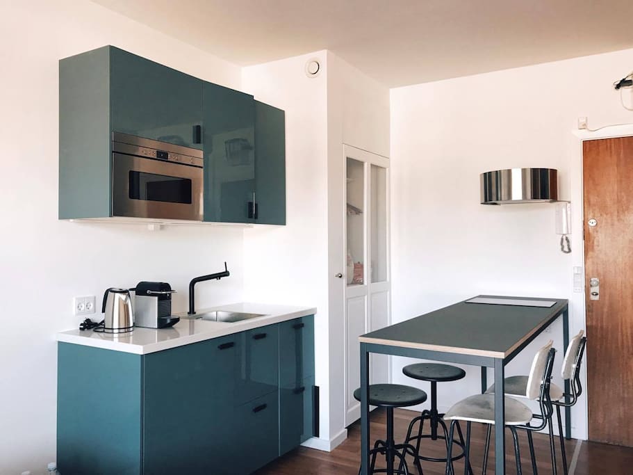 Modern, industrial-designed kitchen with refrigerator, microwave, coffee, tea, hotplate, and a dinner table for four.