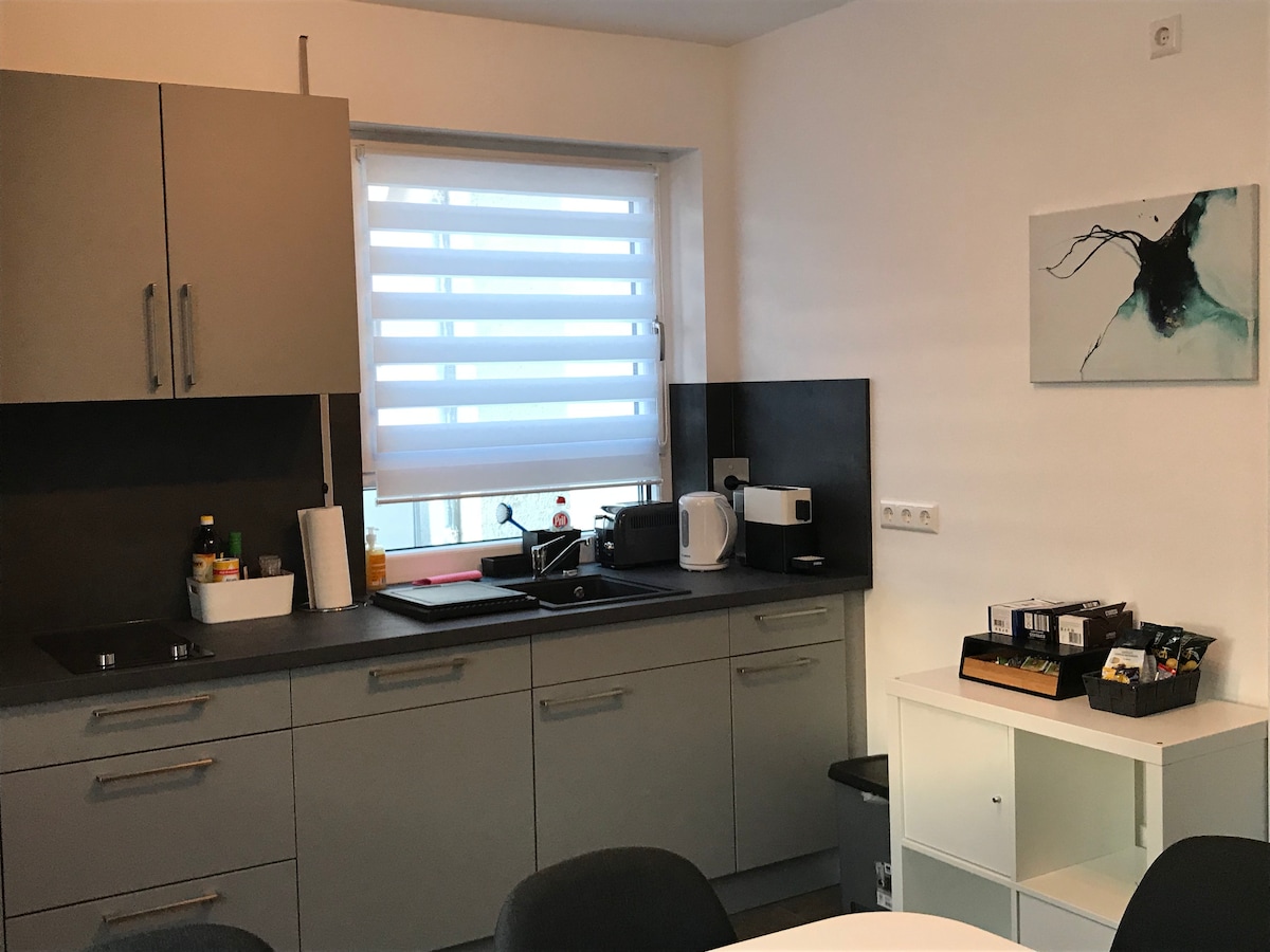 The kitchen features modern cabinetry and a functional workspace. A sink and stovetop are included, along with essential appliances such as a microwave and coffee maker. A window provides natural light, and a wall art piece adds a decorative touch.