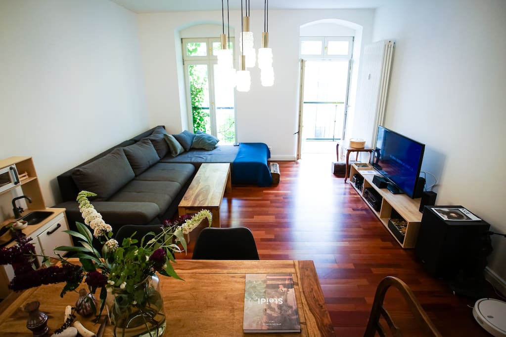 Living room with big couch, TV, dining table and access to the first balcony