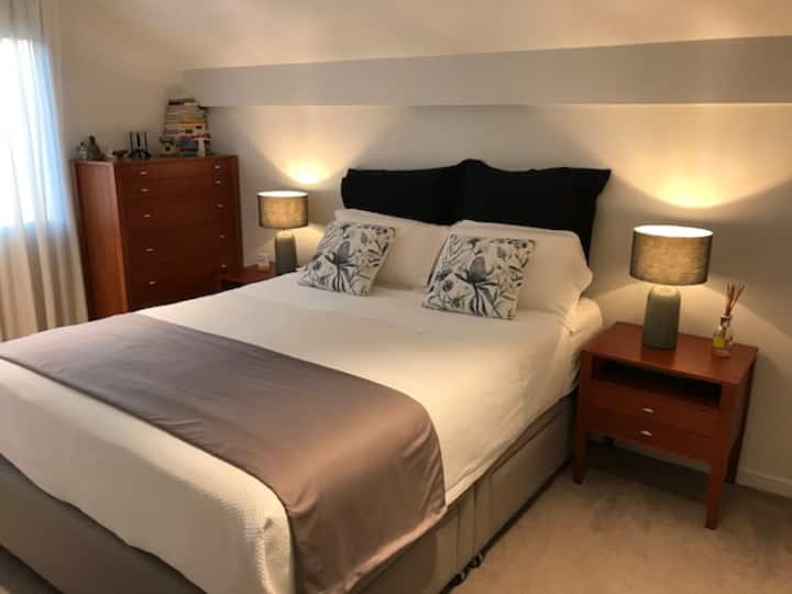 Chumba kikuu cha kulala chenye kitanda na dirisha la ukubwa wa malkia linaloangalia bustani ya nyuma.