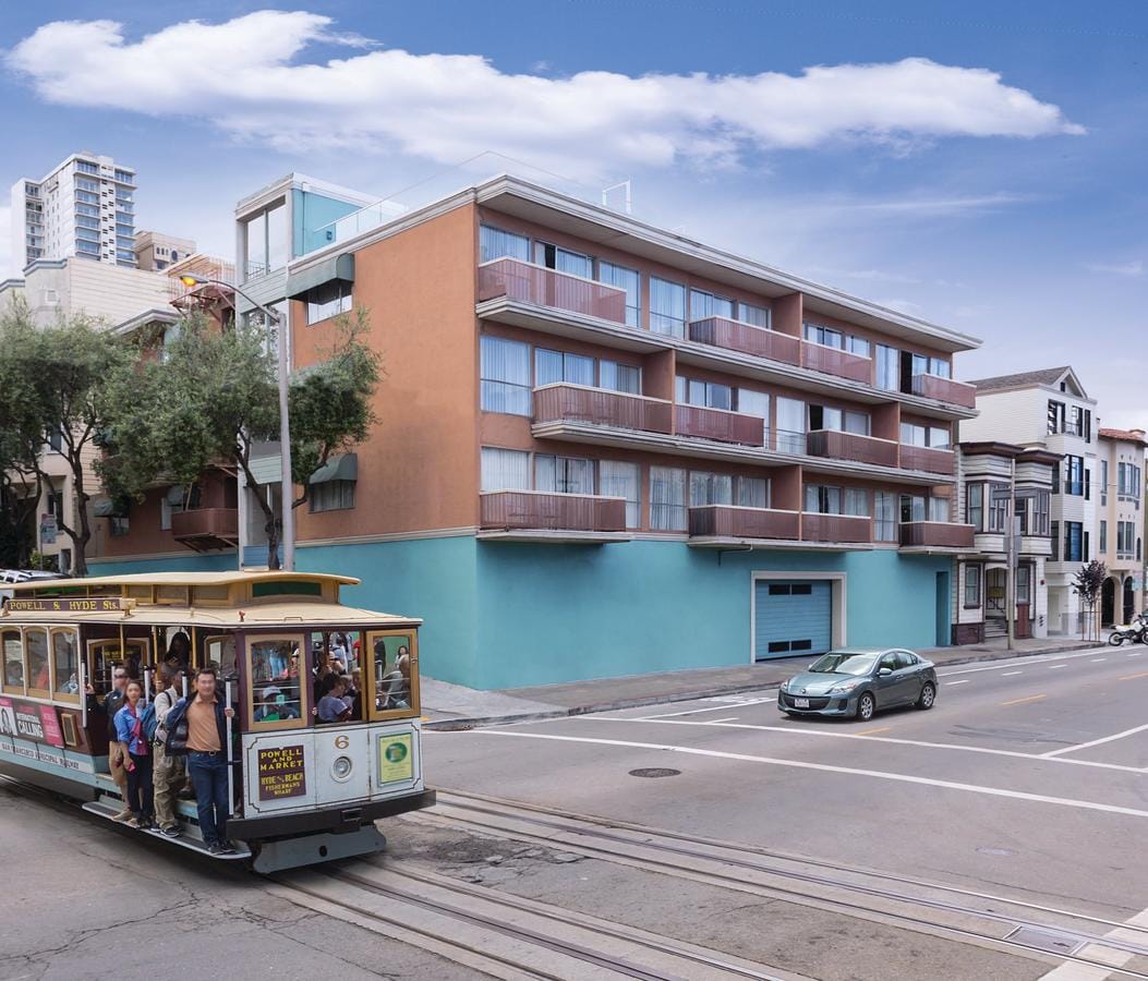 A view of a three-story building featuring a combination of orange and blue exterior walls, situated near a bustling street. A classic San Francisco cable car is seen transporting passengers in front, adding a vibrant urban element to the scene.