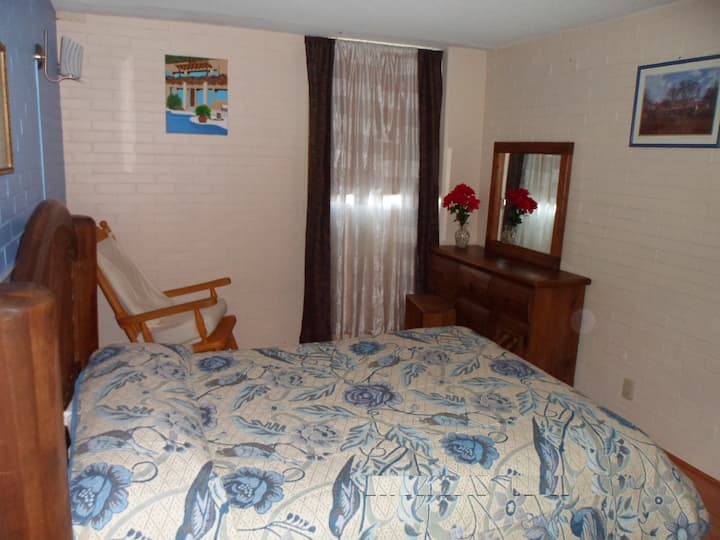 Recámara principial con cama matrimonial, silla mesedora, closet, 2 buros, cajonera con espejo y closet.