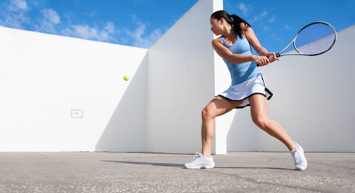 A woman in a blue shirt and white skirt prepares to strike a tennis ball with her racket on the court.