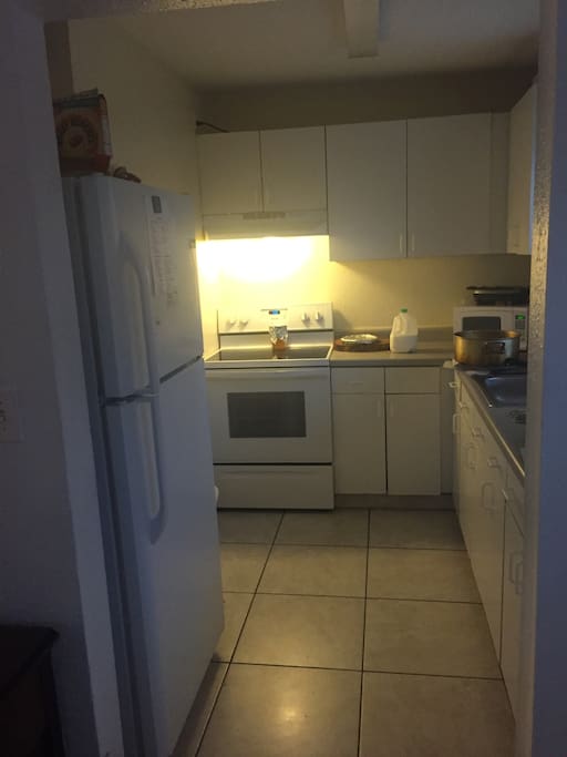 Functional kitchen with a glass top stove, microwave, panini maker & refrigerator.
