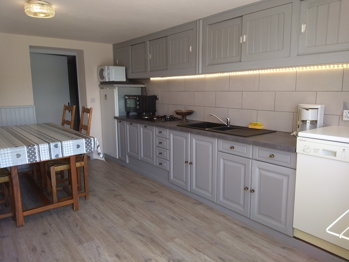 A modern kitchen is showcased with gray cabinetry and under-cabinet lighting. An array of appliances, including a stove, refrigerator, and dishwasher, are visible. A spacious dining table with wooden chairs occupies an adjacent area, contributing to the open layout.