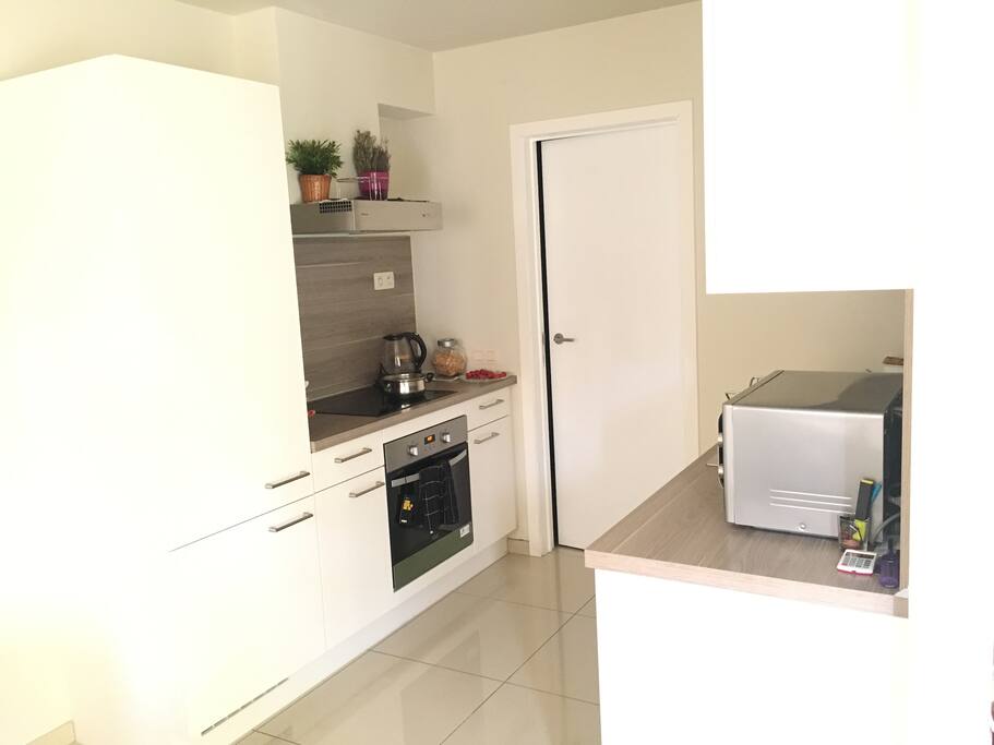 Cuisine américaine ouverte avec micro onde, four électrique, plaque céramique, frigo, garde à manger et ustensiles de cuisine.