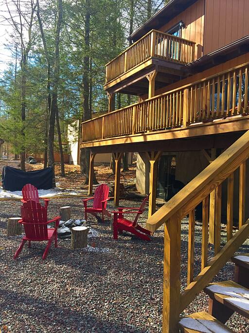 Many outdoor home amenities including a fire pit, gas grill, rocking chairs, and a farmhouse table that seats 14 people.