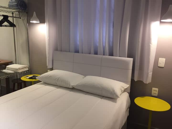 Krevet s okvirom kreveta, pomoćnim stolićima s privjescima i otvorenim ormarom.
