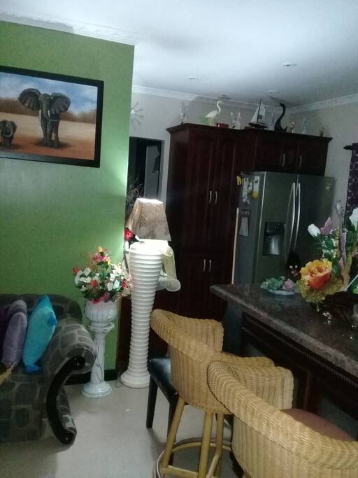 Open concept. Living room, island in kitchen with bar stools, side by side refrigerator with ice maker.