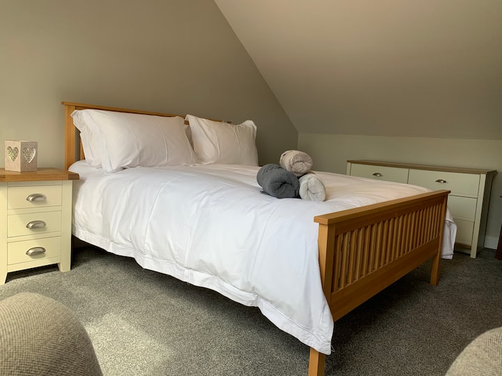 Dormitorio tamaño king en la planta superior con colchón cómodo, ropa de cama de lujo, mucho espacio para guardar cajones y Sky TV.