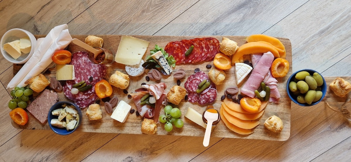 An elegant wooden serving board is filled with a variety of cured meats, cheeses, fruits, and olives. Featured items include slices of salami, prosciutto, and a selection of soft cheeses, complemented by grapes, dried apricots, and crackers, enhancing the inviting dining experience.