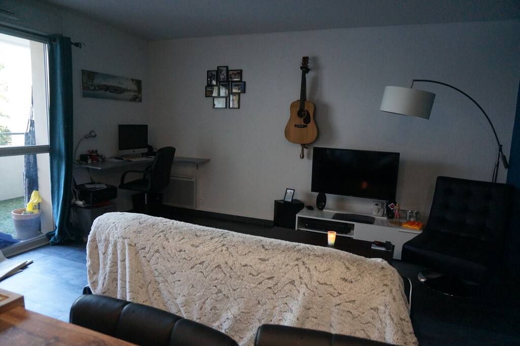 Salon avec TV, canapé, guitare et bureau.