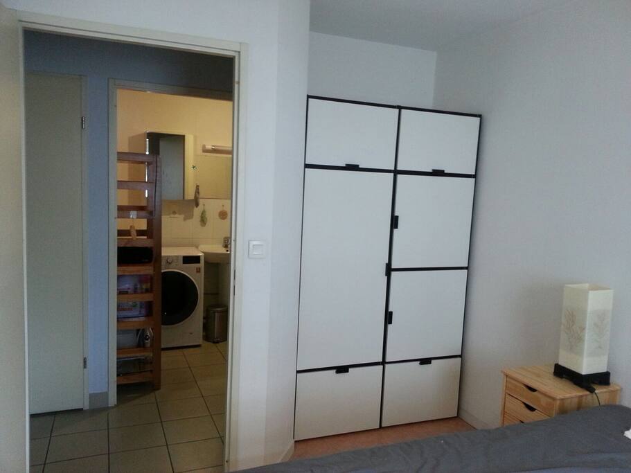 Vue de la salle de bain (sanitaire à gauche de celle ci) depuis la chambre. Armoire avec penderie à droite
