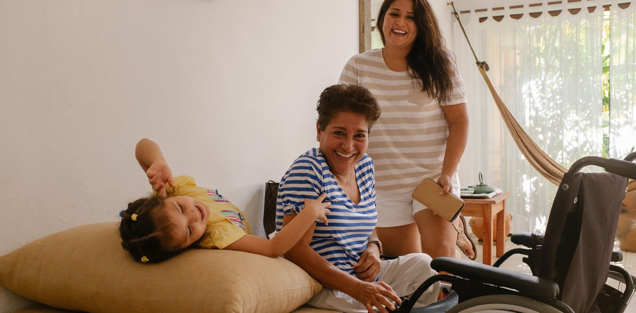 Drei Generationen einer Familie lachen in einer barrierefreien Unterkunft auf Airbnb. Vor dem ältesten Familienmitglied steht ein Rollstuhl.