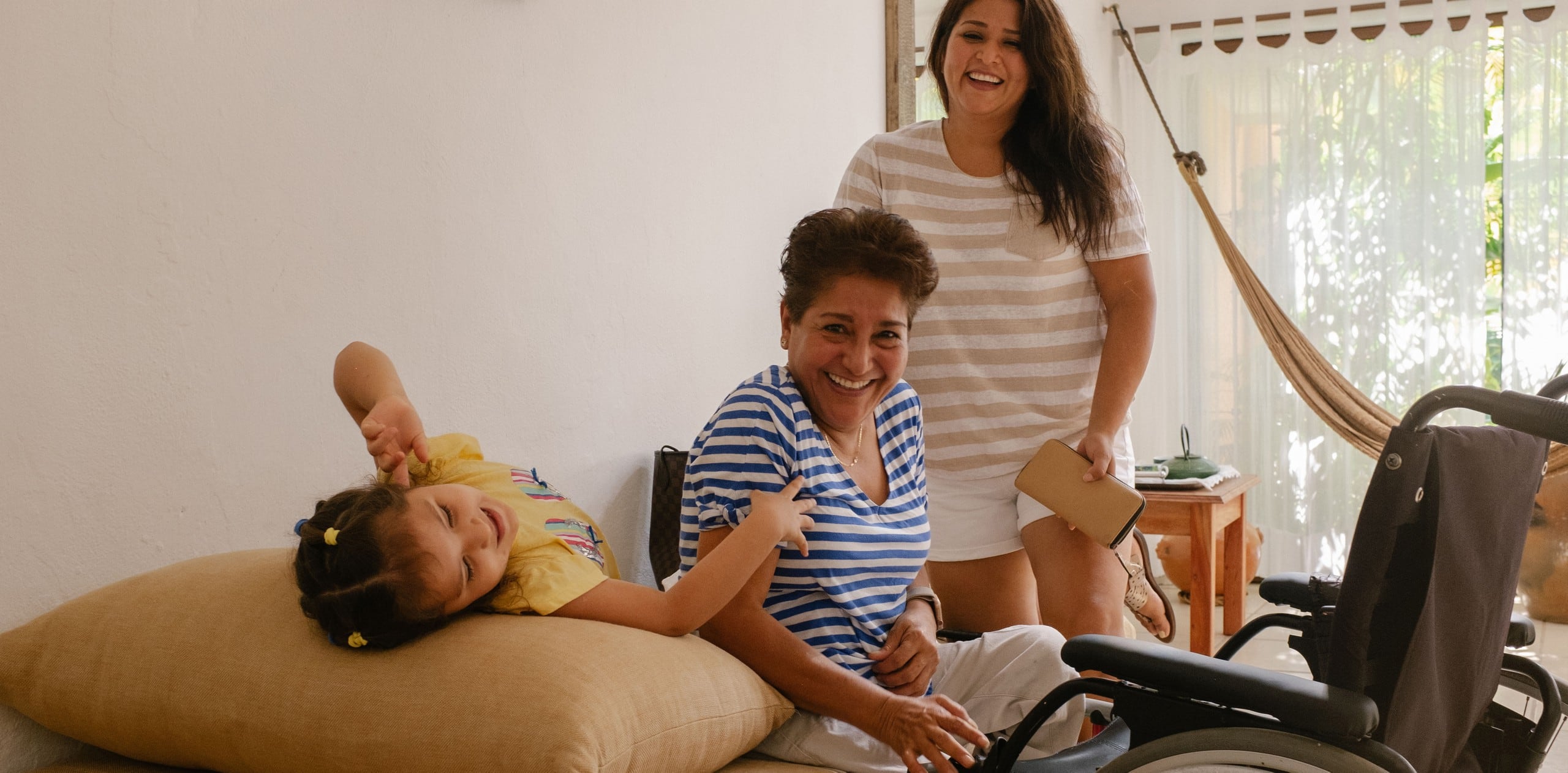 Three generations of a family are smiling and laughing in an accessible Airbnb home. In front of the oldest family member is a wheelchair.