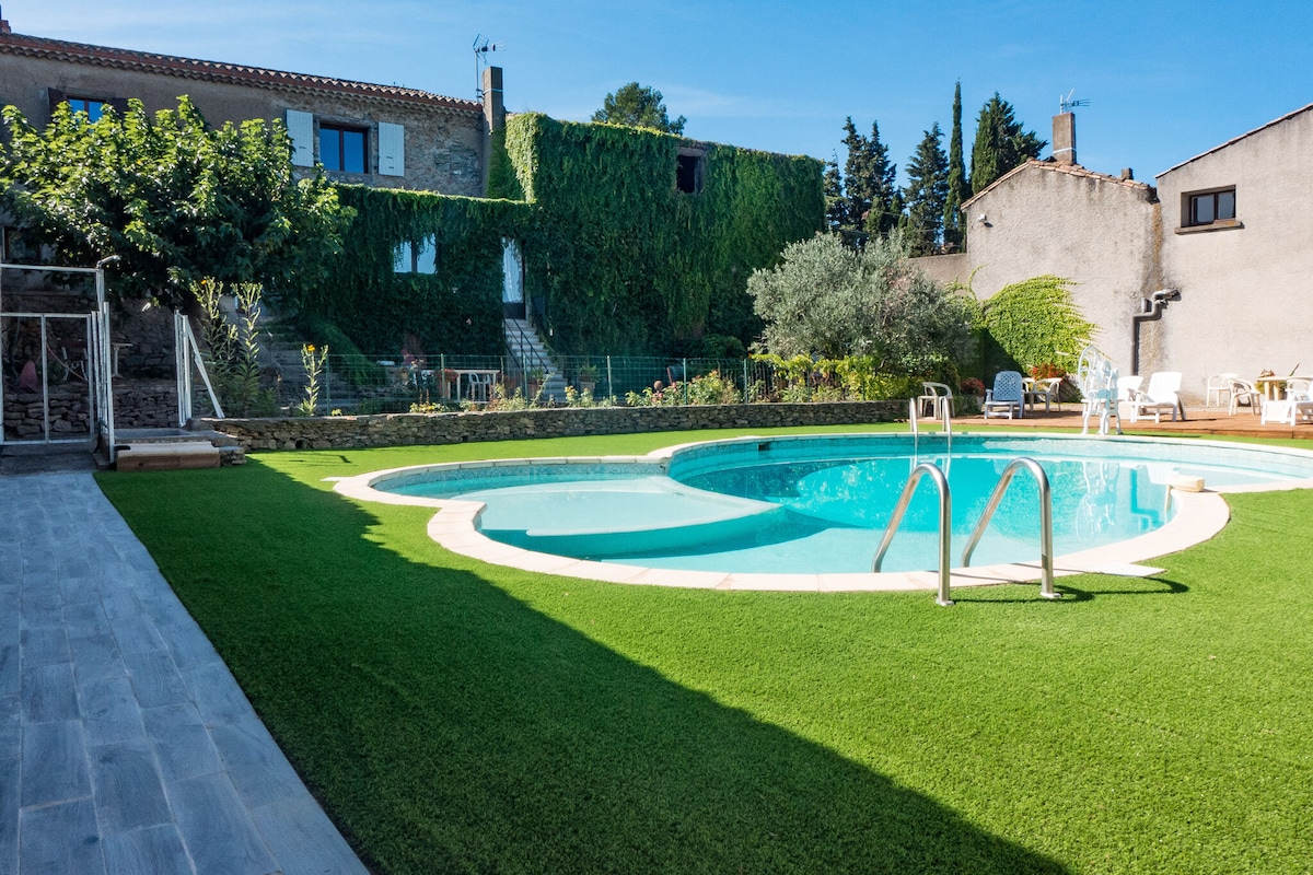 The shared swimming pool features three distinct sections, designed for both children and adults. Surrounding greenery and lounge chairs offer relaxing outdoor space. Fenced for safety, the pool area includes well-maintained grass and is accessible from the cottage.