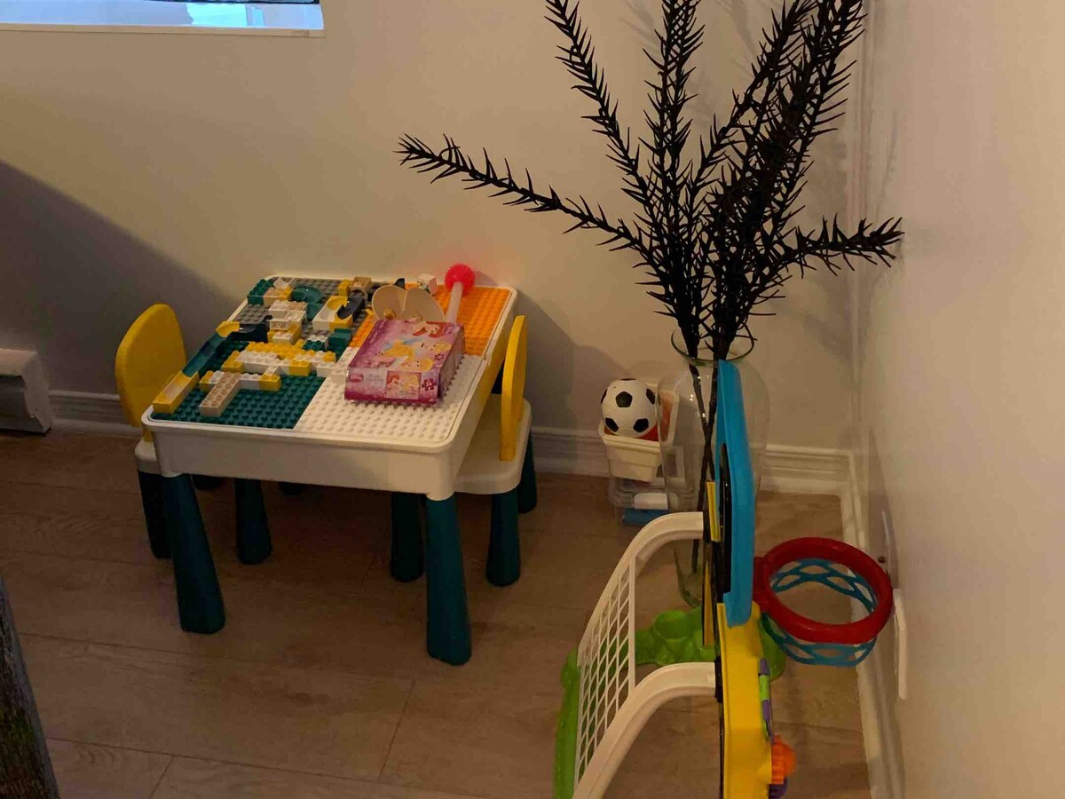 A child-friendly play area is provided with a small table and colorful chairs, complemented by building blocks and a few toys. Nearby, a small basketball hoop stands next to a potted plant, creating an inviting space for playful activities.