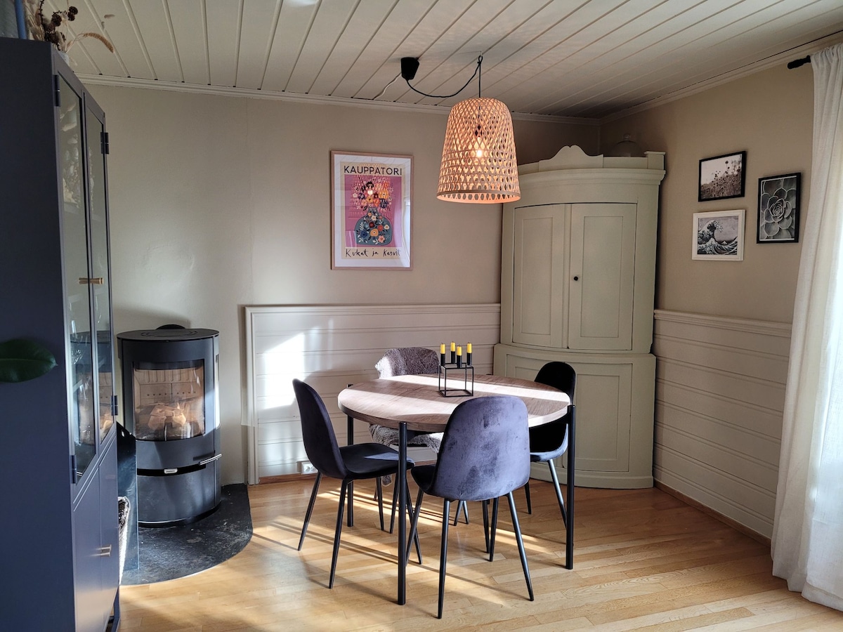 A dining area features a round table surrounded by four dark chairs. A white decorative cabinet stands nearby, while a pendant light casts a warm glow. The room is enhanced by a small fireplace and framed artwork adorning the walls.
