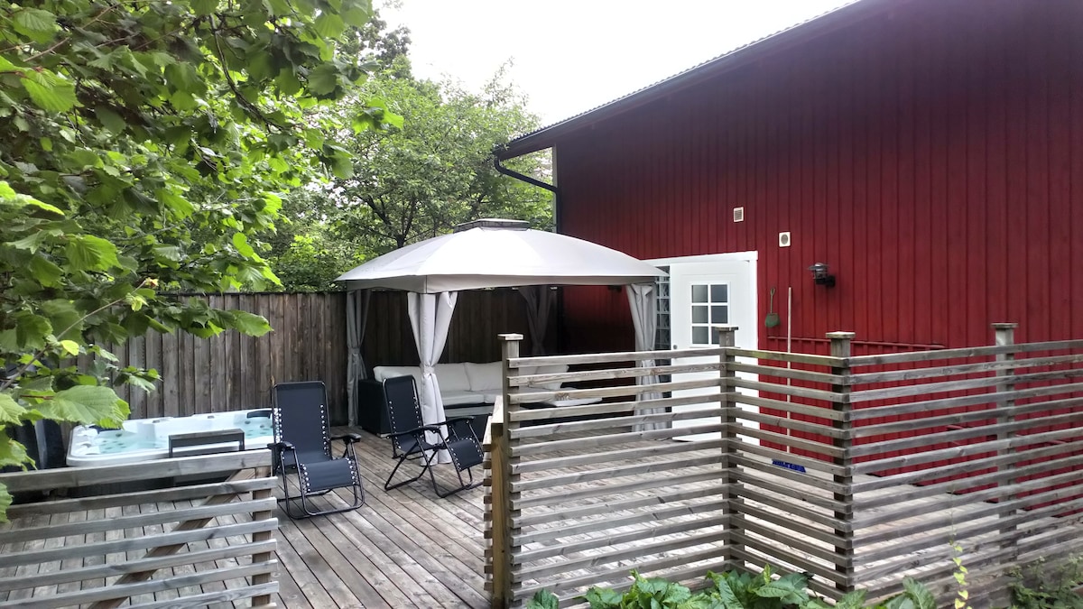 A private outdoor terrace is enclosed by wooden fencing, featuring a gazebo. Two lounge chairs and a seating area are visible, with a hot tub nearby. Lush greenery surrounds the space, enhancing the feeling of privacy and tranquility.