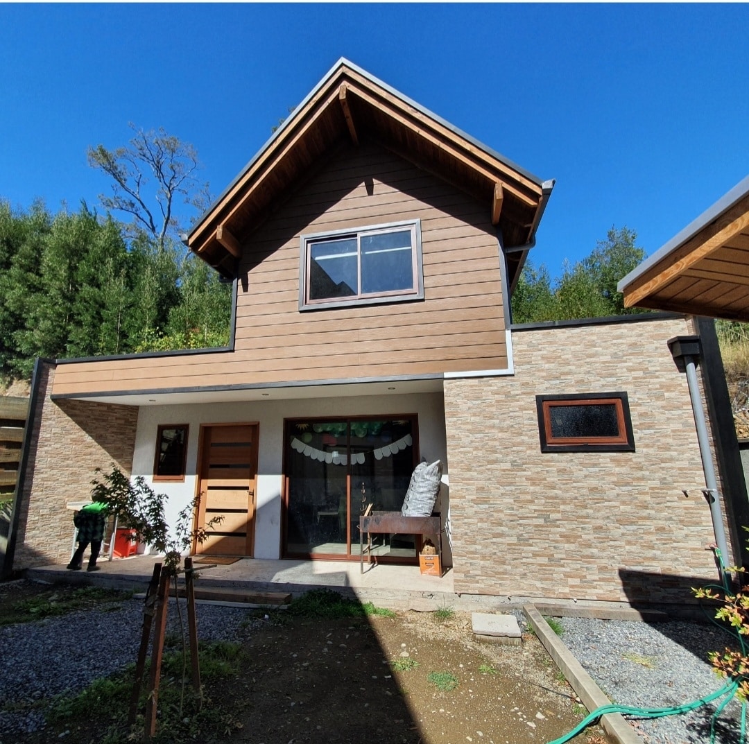 A two-story house is presented, featuring a combination of wooden accents and stone facade. The broad front porch includes a sitting area, and large windows allow for abundant natural light. Surrounding greenery enhances the residential setting.