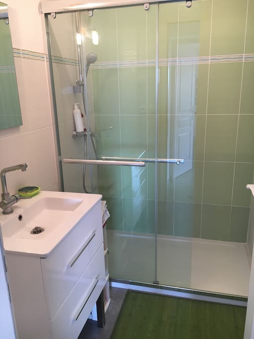 Salle de bain claire avec grande douche et sèche serviettes.