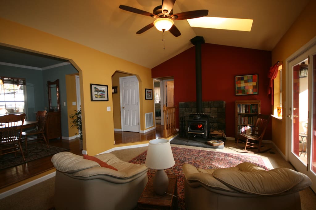 LIving room with full view of deck, wood stove, ceiling fan, and skylights. For short stays, this can be your own private space if desired.