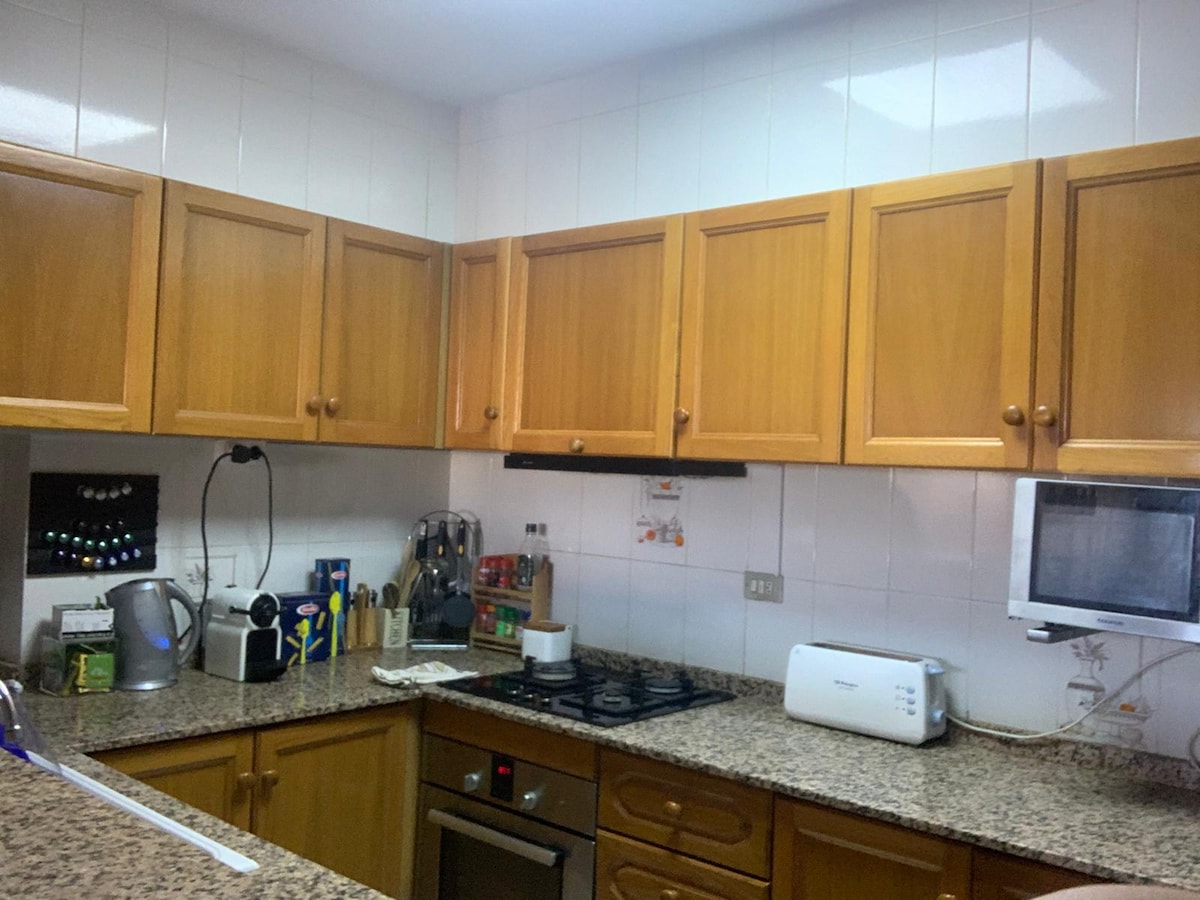 The kitchen area features wooden cabinetry, providing ample storage. A countertop is finished in speckled stone, with various appliances including a toaster, kettle, and microwave. The gas stove is positioned beneath a ventilation hood, enhancing the functionality of this space.