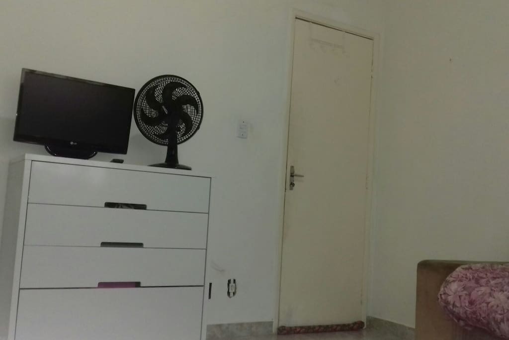 cômoda com 4 gavetas, televisão e ventilador. Porta com ganchos