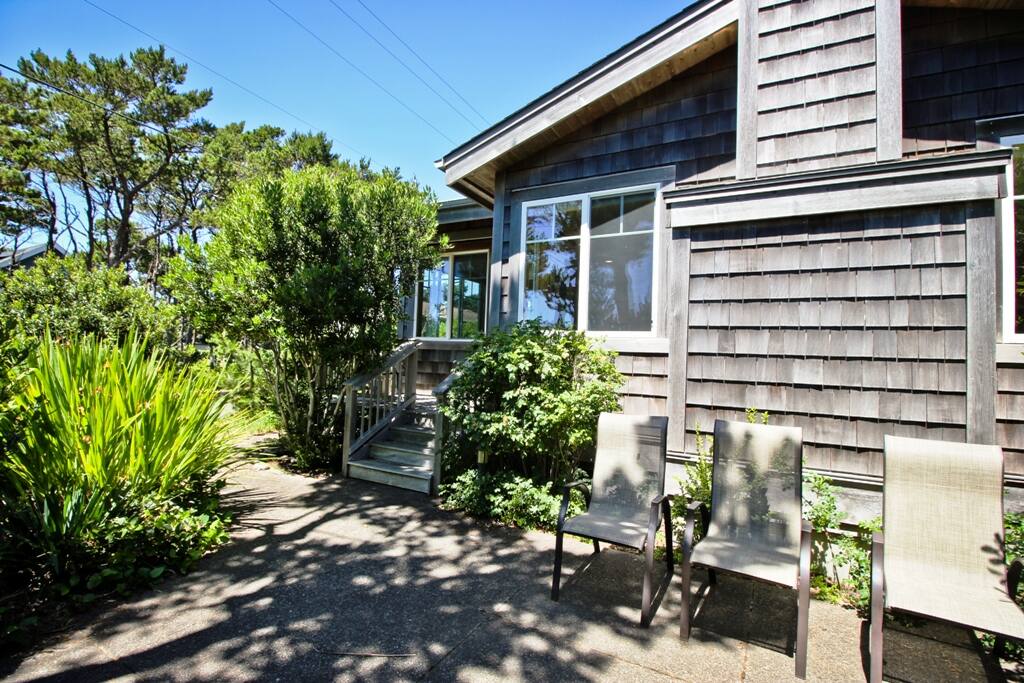 Front view of Valentines House. Landscaped yard with a stone patio, chairs and gas BBQ.