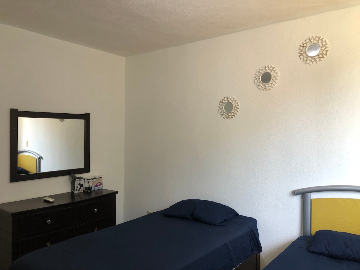 Second bedroom features two twin beds with air conditioning, dresser with mirror and drawer , iron and dryer .