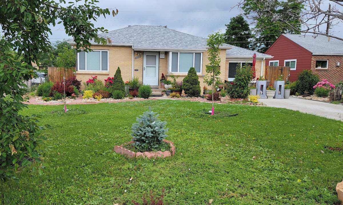 A well-maintained front yard features a manicured lawn surrounded by colorful flower beds and shrubs. A pathway leads to the inviting entrance of the house, which is complemented by a neutral-colored facade. The area is dotted with decorative plants and trees, enhancing the outdoor space.