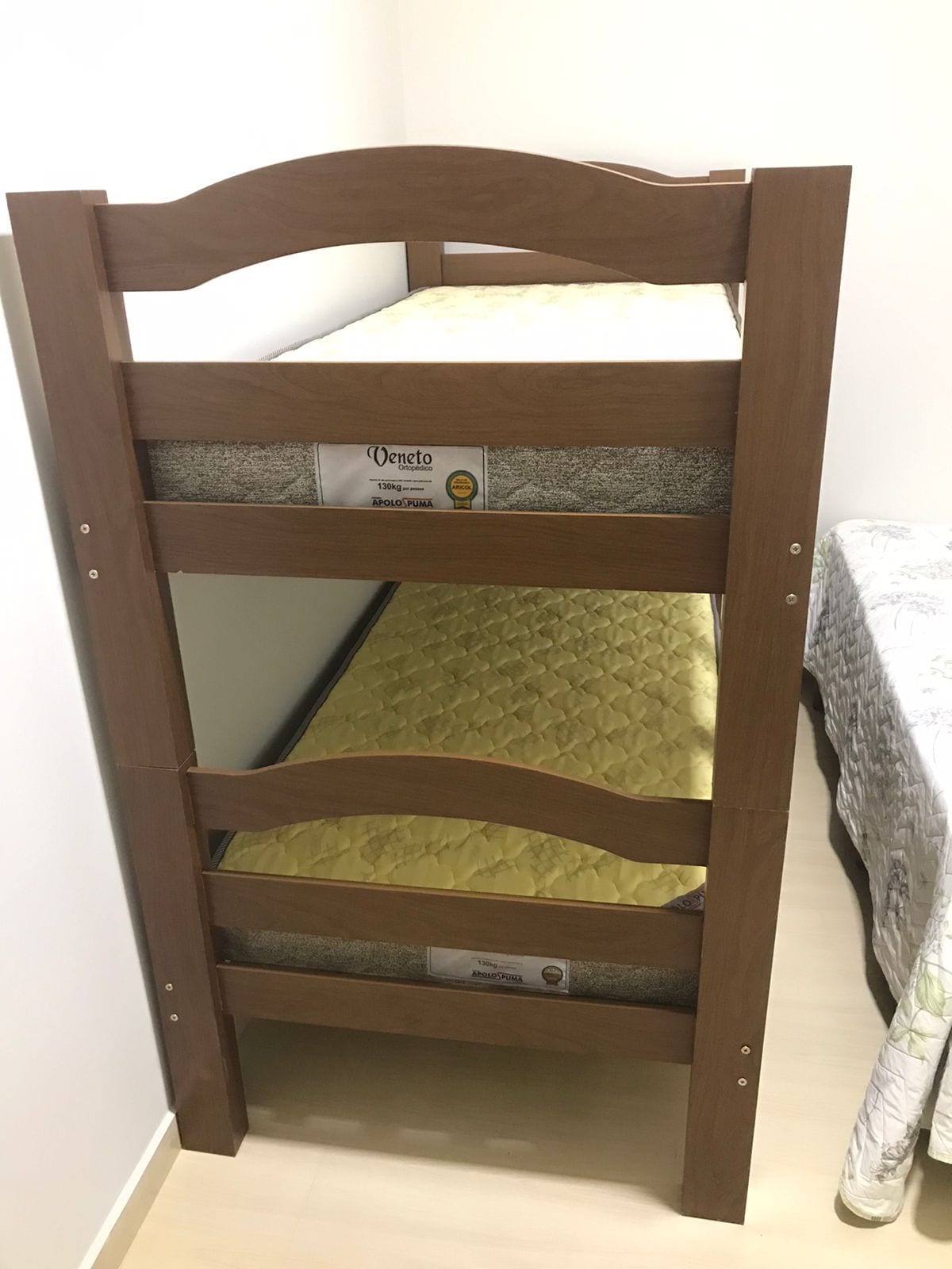 A wooden bunk bed is displayed in the image, showcasing two neatly made mattresses with golden covers. The top and bottom bunks are visible, indicating a compact design suitable for maximizing space.