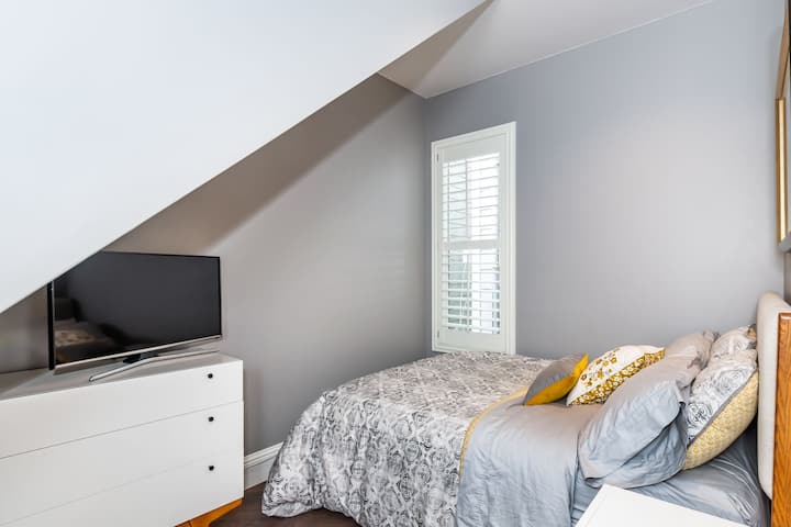 Segundo dormitorio con cama tamaño queen, TV, cómoda y mesita de noche.