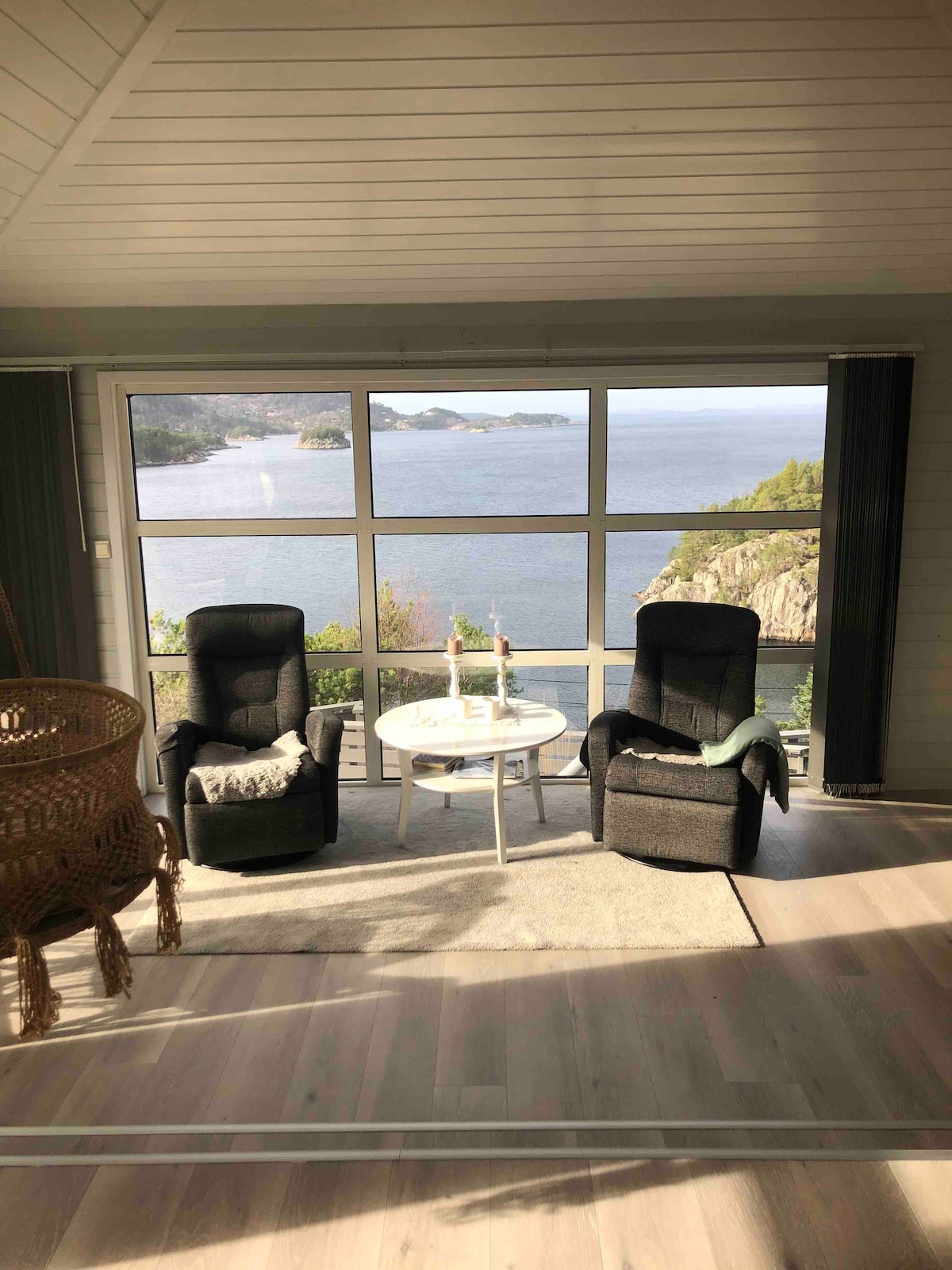 A light-filled sitting area features two comfortable armchairs facing a large window with stunning views of the water and surrounding landscape. A small round table is placed between the chairs, creating an ideal space for relaxation and enjoying the scenery.