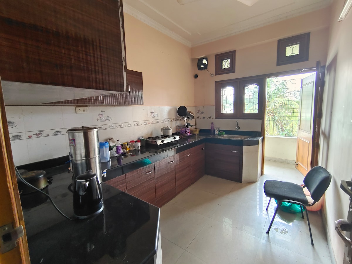 The kitchen features a modern design with dark wood cabinetry and black countertops. Various utensils and appliances are organized on the counters. A window allows natural light, complementing the accessible layout with space for movement.