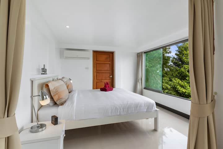 Serene guest bedroom with crisp white linens, air conditioning and garden-facing windows providing natural light